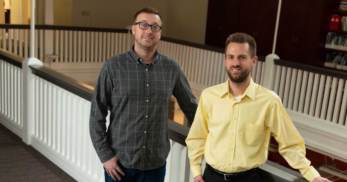 two men standing in front of white railing smiling
