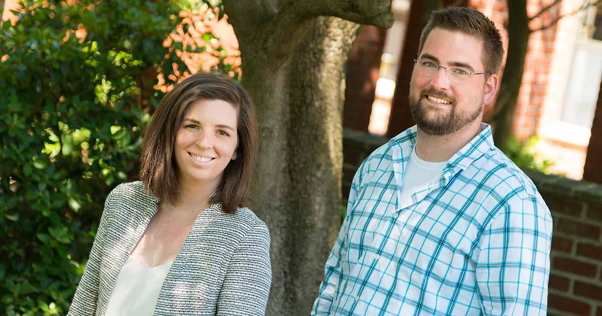 Two employees in front of tree