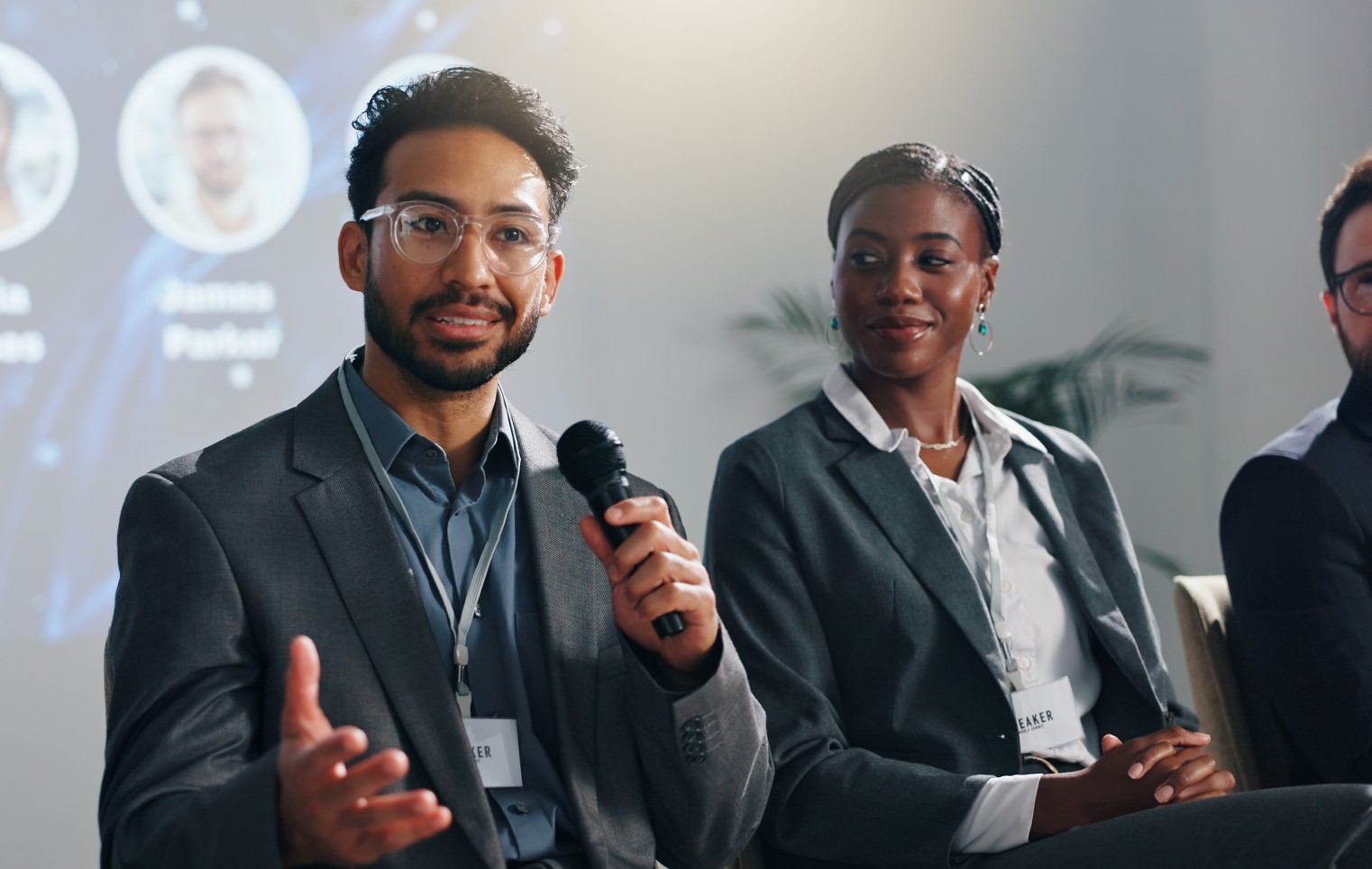 Business professional speaks into a microphone during a conference panel while fellow speakers listen, highlighting thought leadership and industry discussion.