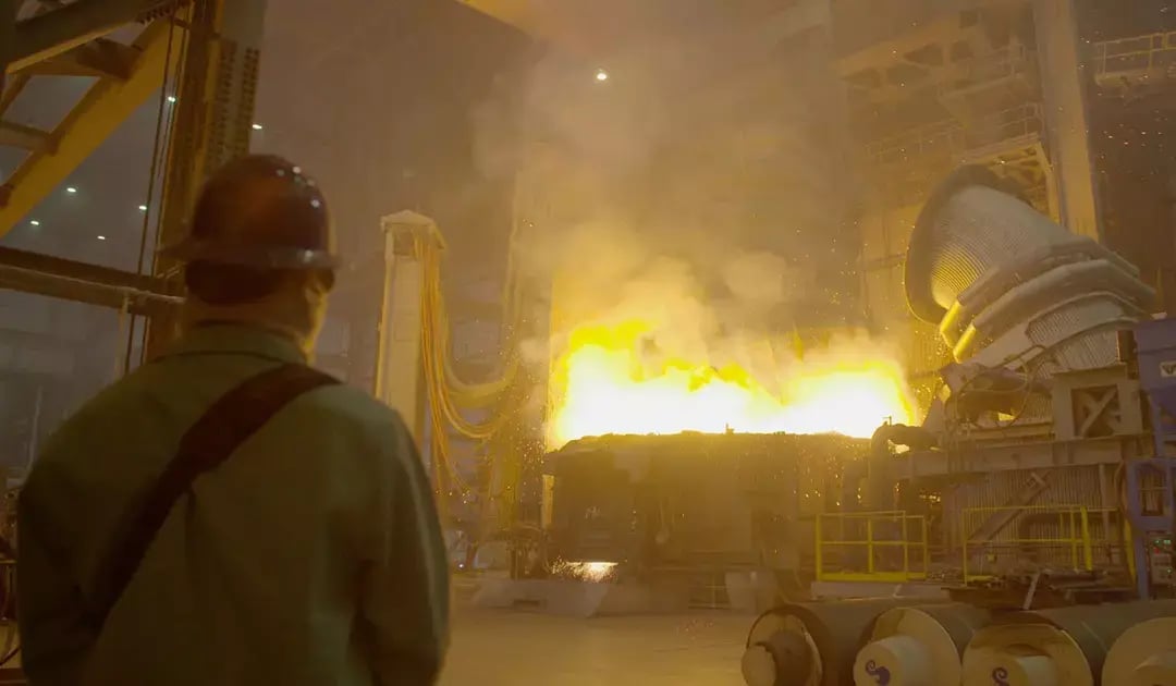 Steel mill worker watches glowing molten steel and heavy industrial equipment inside the Big River Steel facility.