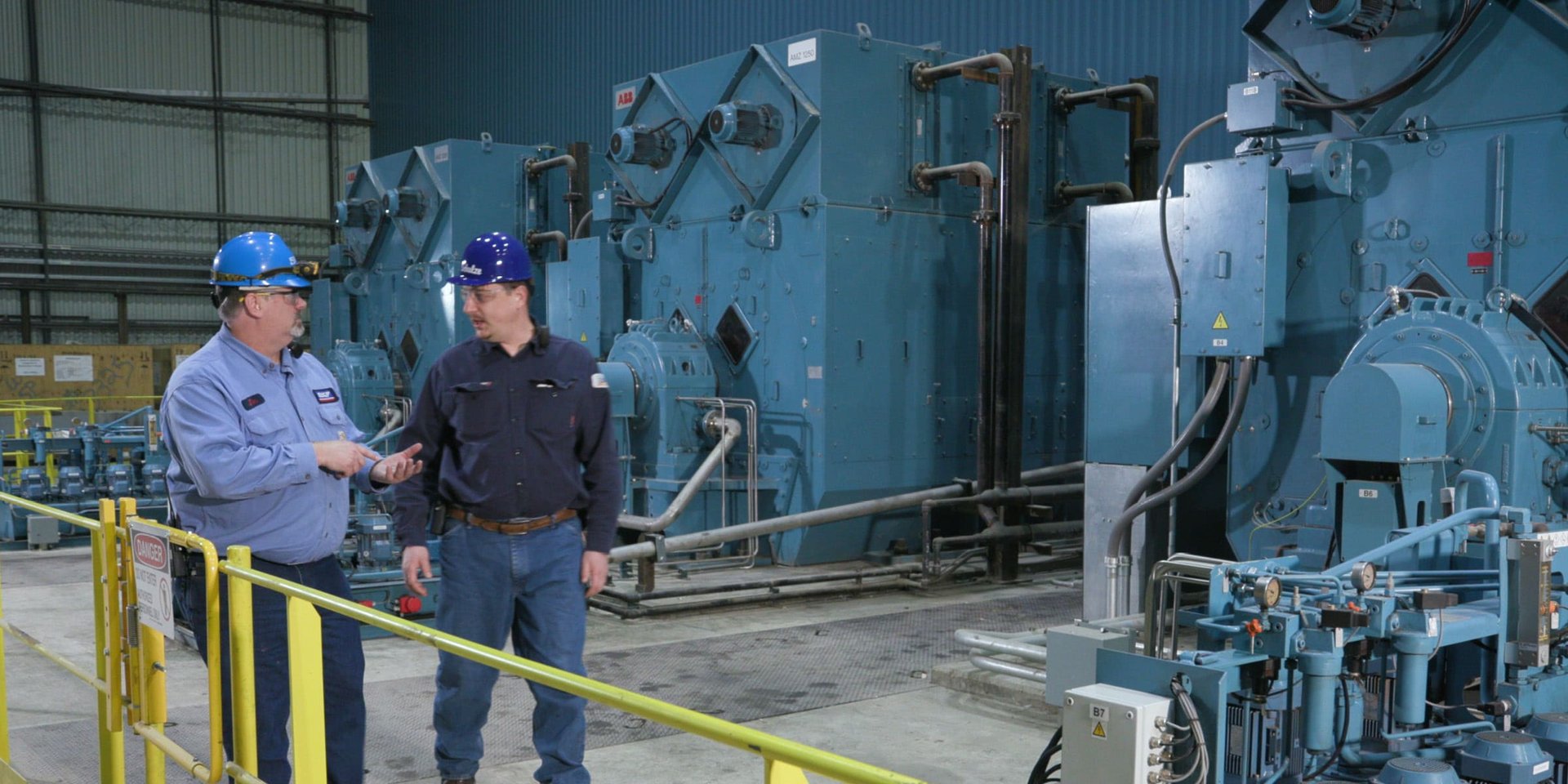 Two workers in hard hats talk beside large industrial machinery inside the Big River Steel facility.