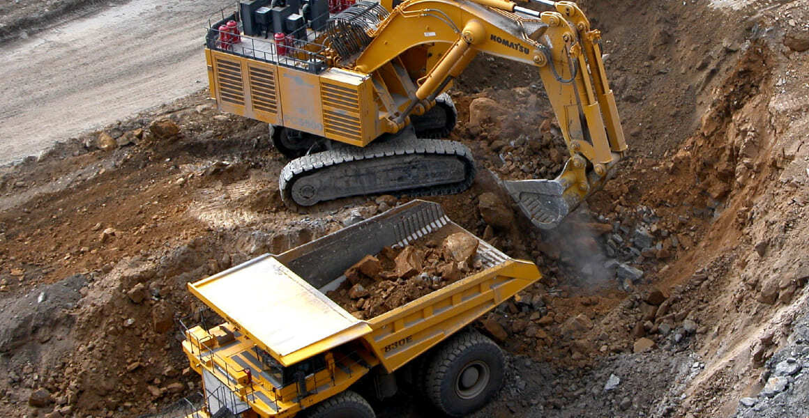 Large excavator loads rocks into a mining haul truck at an open-pit mine.