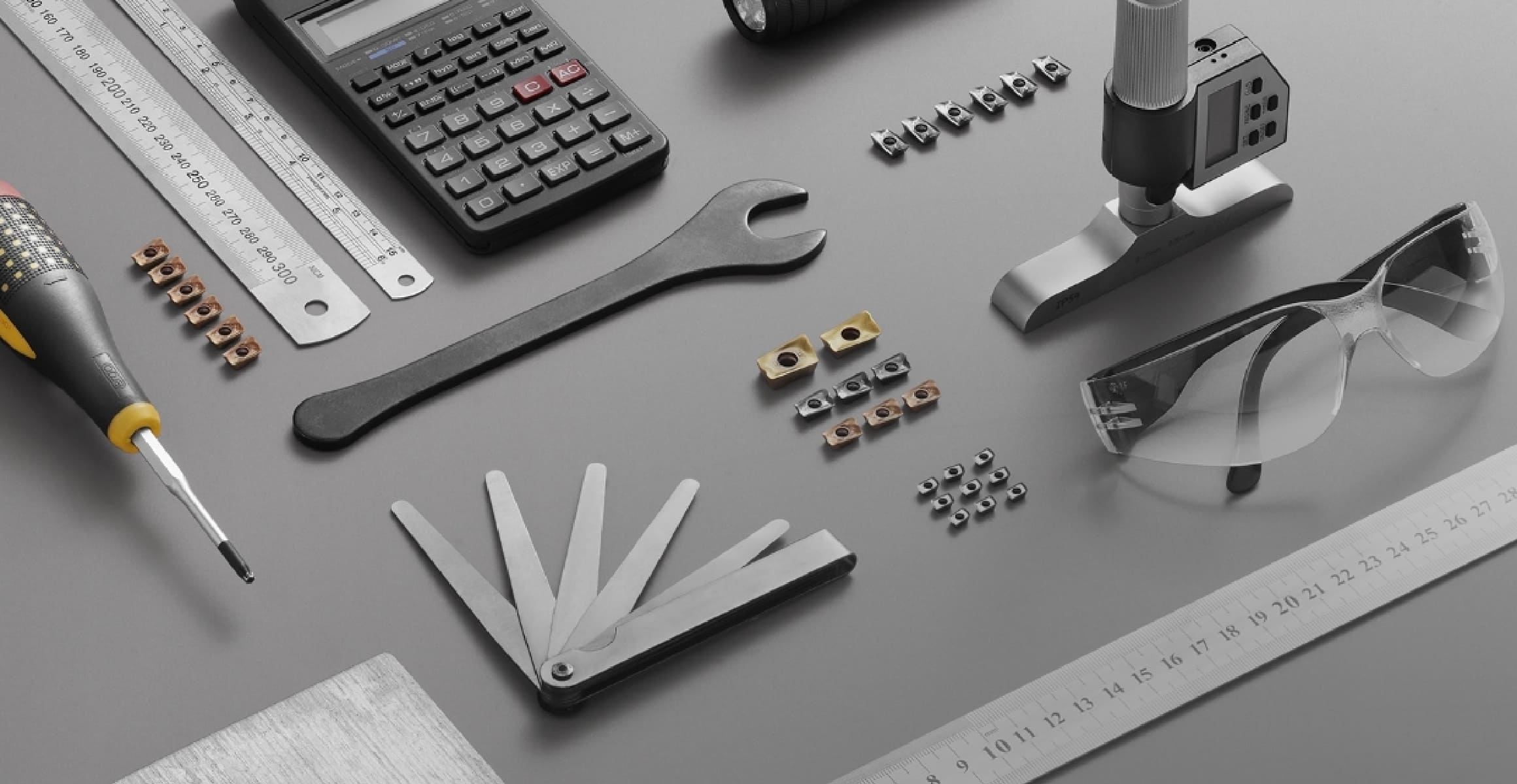Machining tools and equipment arranged on a workbench include rulers, cutting inserts, a wrench, gauges, safety glasses and screwdriver.