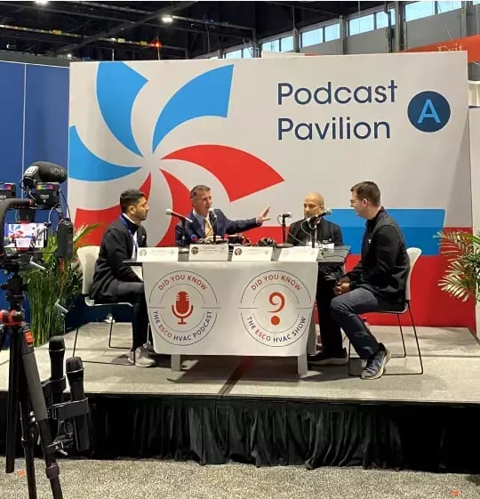 Four HVAC professionals record a live industry podcast on stage in the Podcast Pavilion during the AHR Expo trade show with video cameras.