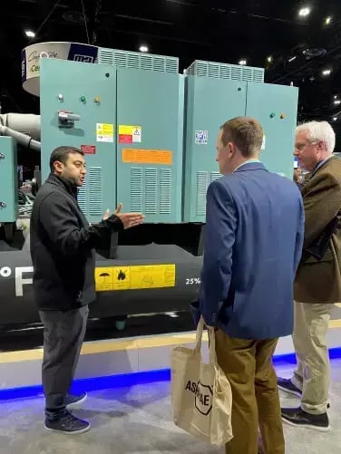 Johnson Controls representative discusses a large YORK chiller with two attendees during a product demonstration at the AHR Expo trade show.