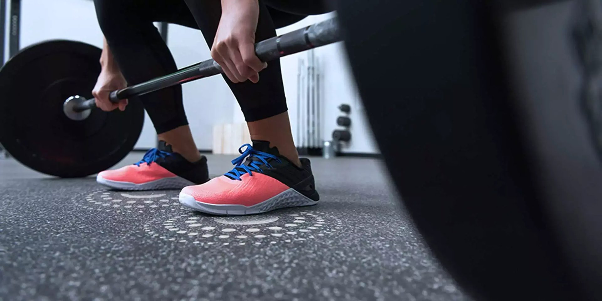 Athlete lifts a barbell on speckled Ecore performance flooring while wearing bright training shoes.