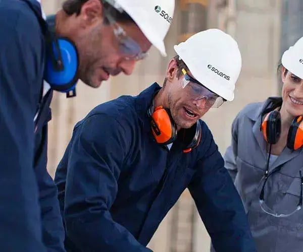 Two mining professionals wearing hard hats and safety gear review information together at an industrial mining site.