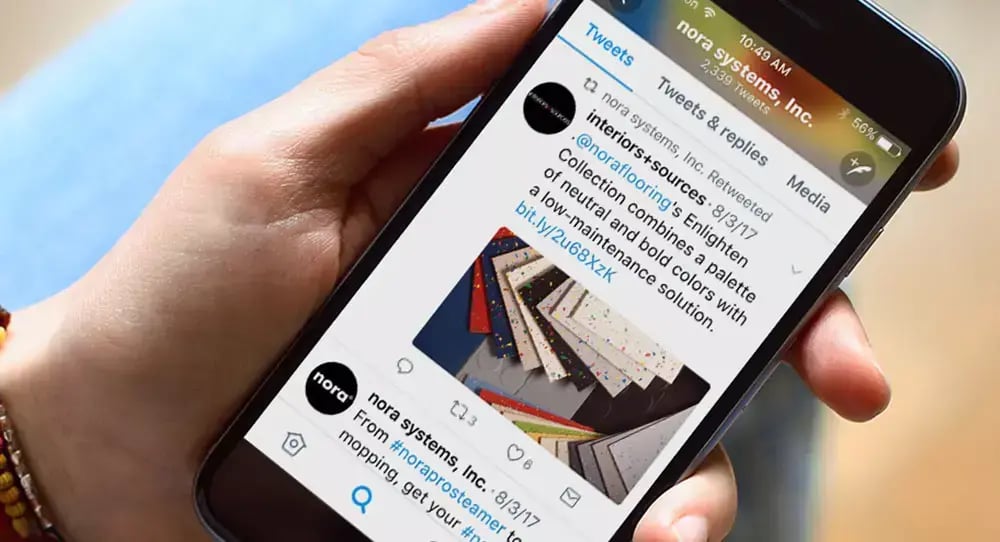 Person holding a smartphone displaying a nora systems social media post featuring colorful rubber flooring samples and product information.