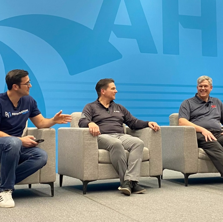 Three industry professionals seated onstage during a panel discussion against a blue AHRI-branded backdrop.
