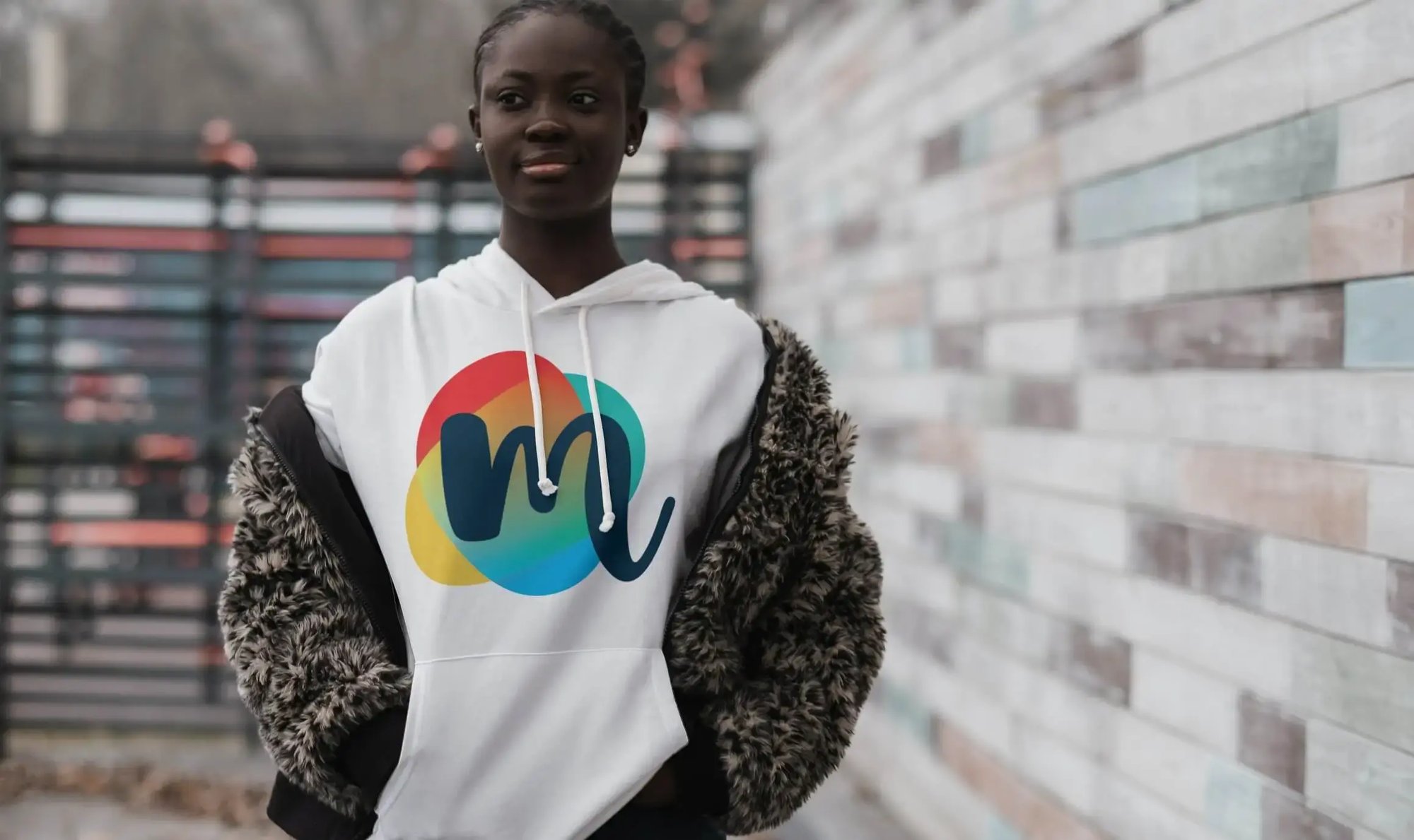 Young woman wears a white hoodie featuring The Mix colorful logo, demonstrating the youth organization’s refreshed visual identity.