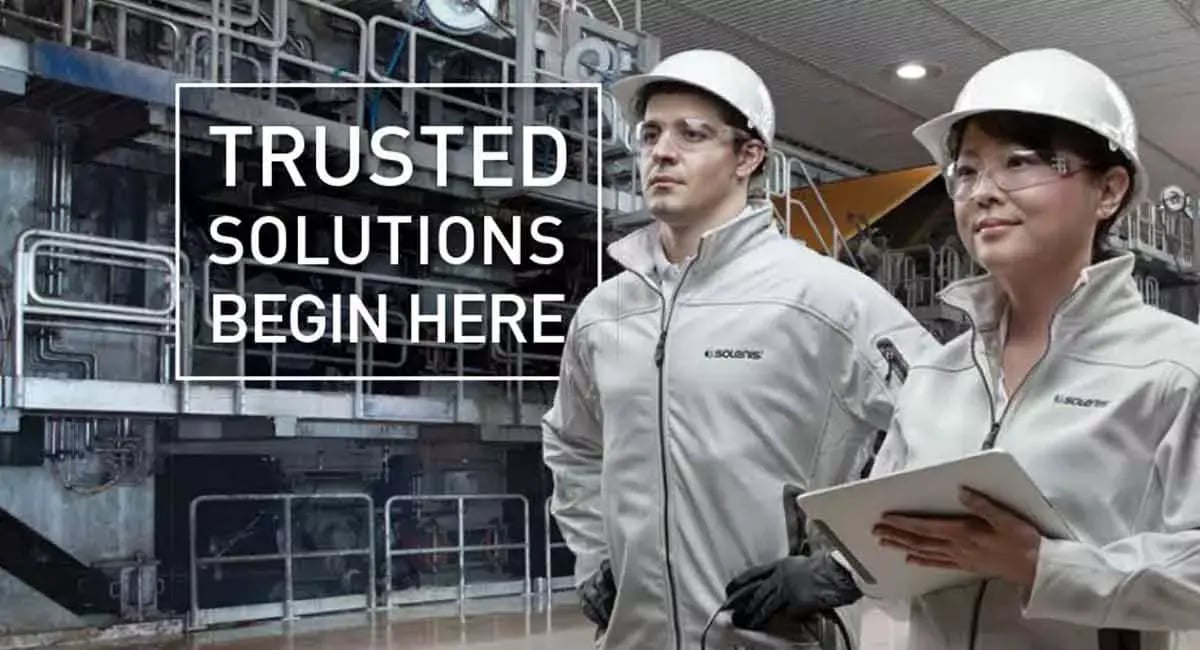 Two Solenis team members wearing safety gear stand inside an industrial facility beside the message “Trusted solutions begin here.”