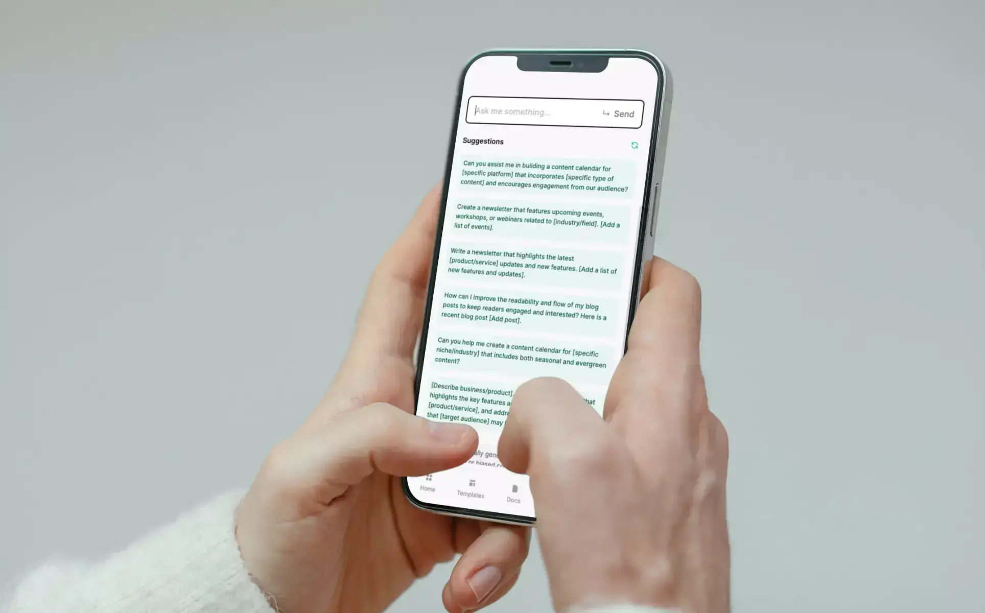 Hands hold a smartphone displaying an AI writing assistant with suggested prompts for content calendars, newsletters and blog posts.